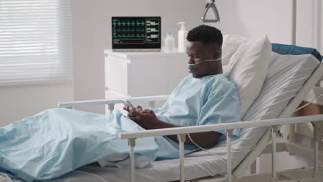 A-black-man-is-lying-on-a-hospital-bed-and-plowing-a-message-to-his-friends-and-relatives-from-the-hospital.-Communication-with-loved-ones-in-the-hospital-via-the-Internet-and-mobile-devices